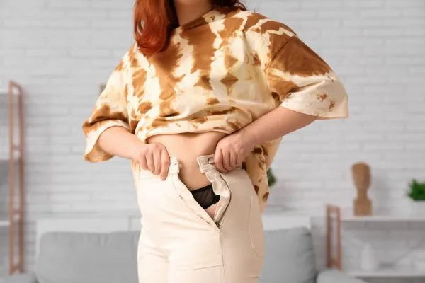 Image of woman trying to do her trousers up after pregnancy weight gain Harlow
